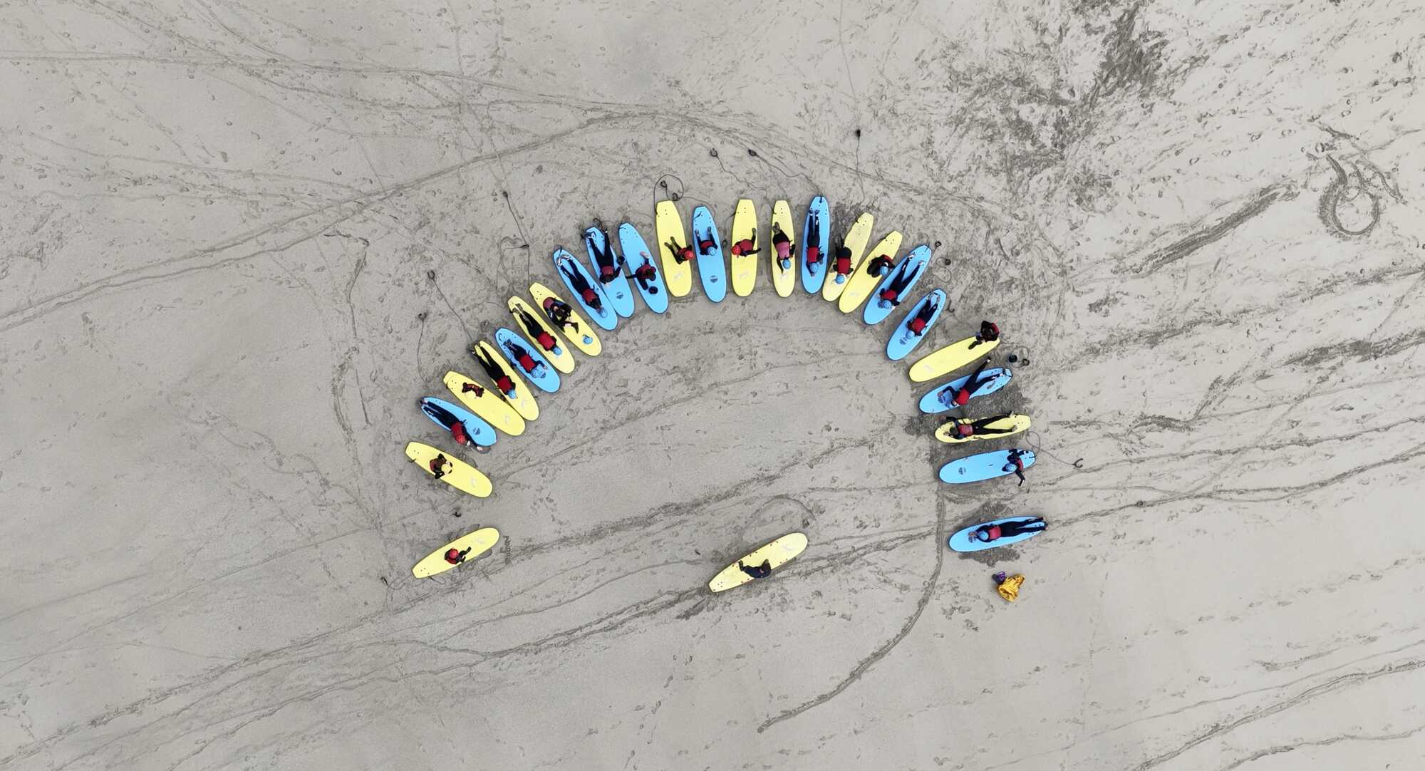 Students and their surfboards arranged in a circle on the sand during a beach briefing.