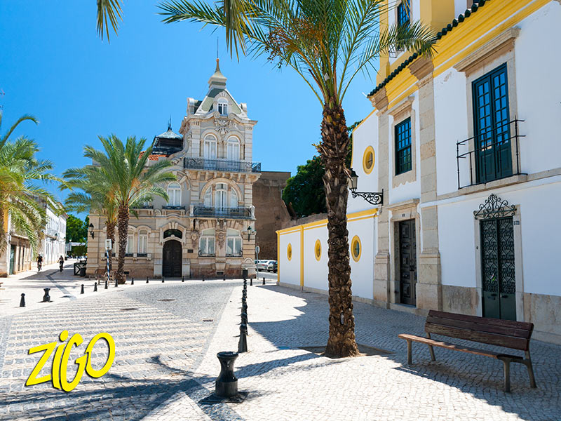 Paved square in the old town of Faro with whitewashed buildings, palm trees and a bench