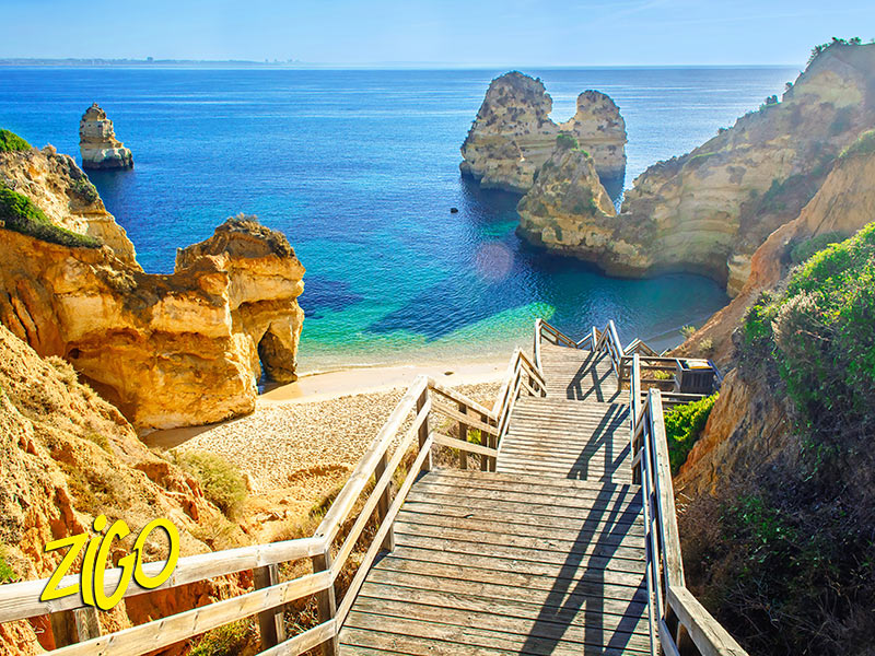 Wooden stairway leading down to a sandy cove enclosed by golden cliffs and sea stacks
