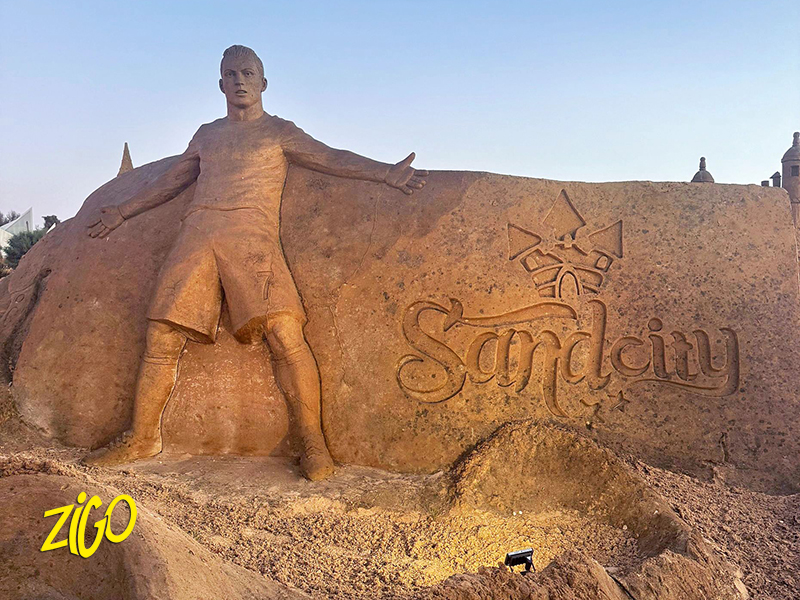 Large sand sculpture of a standing figure beside the carved word Sandcity at the sculpture park