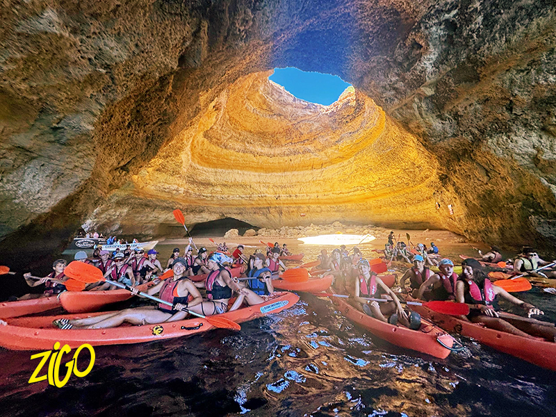 Group of kayaks gathered on the sand inside the Benagil sea cave, daylight falling through the opening in the roof