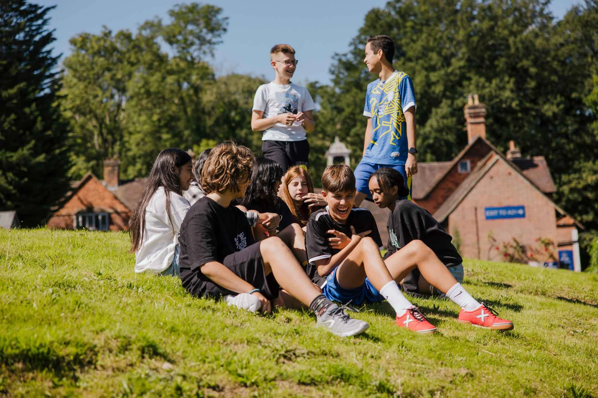 Students sitting on the grass beside a red-brick building at Claremont Summer School