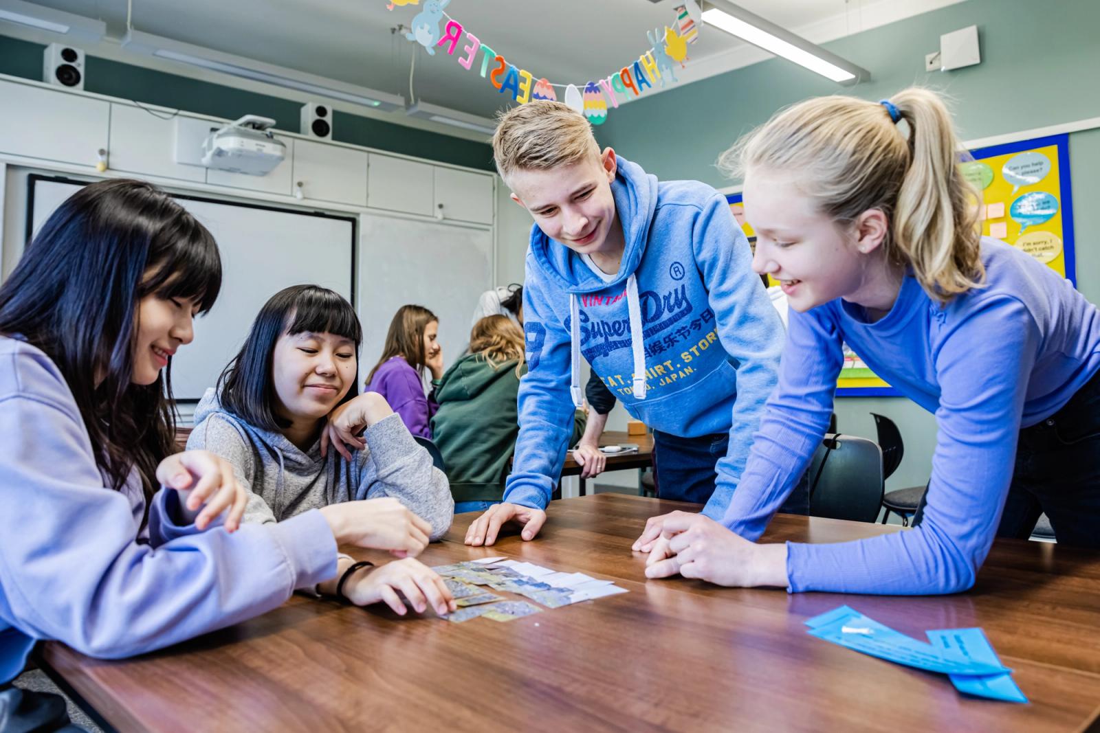 Students and course staff working together around a classroom table at Mill Hill School, London