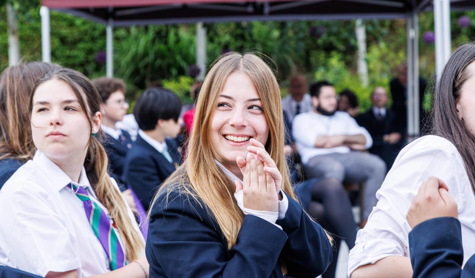 Students seated outdoors under a canopy at a campus event, Mill Hill School, London