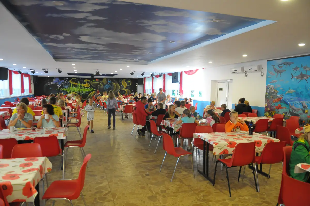 Children eating at tables in the large dining hall of the holiday village