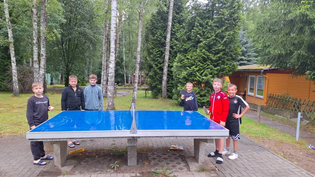 Children standing around an outdoor table tennis table
