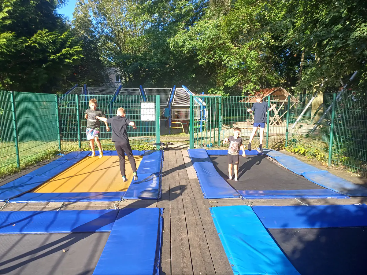 Children jumping on ground-level trampolines inside a fenced area