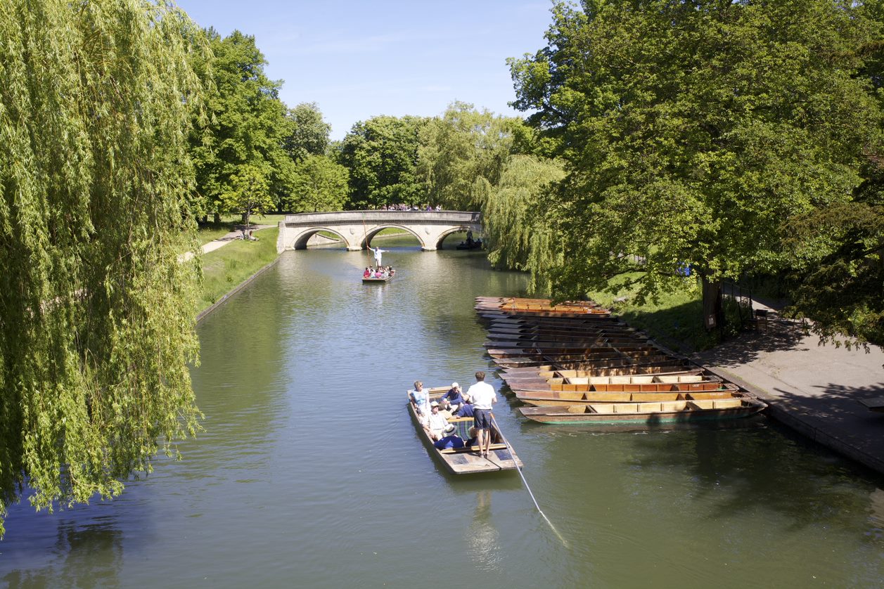 Punts on the River Cam passing under a stone bridge between willow trees, one of the activities on the programme