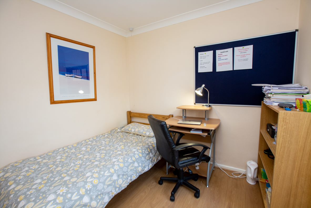 Single study bedroom in a residence with a bed, desk, chair and noticeboard