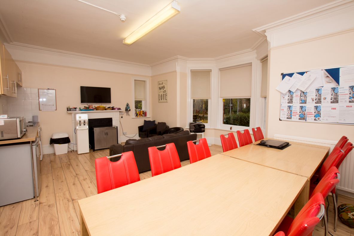 Student common room in a Select English residence with a long dining table, red chairs, television and kitchen area