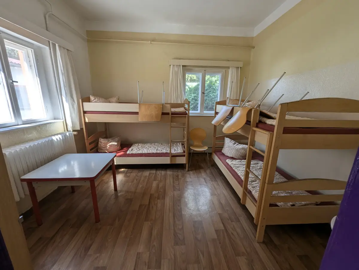 A bedroom with wooden bunk beds, a low table and a curtained window at the Prieros camp