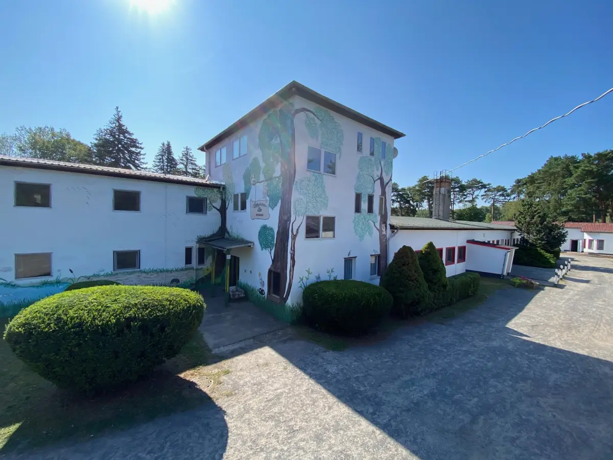 The white two-storey accommodation house with a painted mural, clipped hedges and a paved yard in front