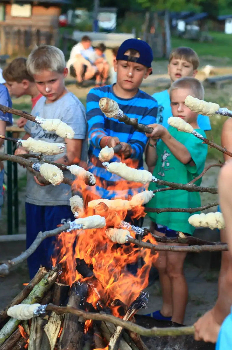 Children holding long sticks wound with bread dough over the camp fire at Prieros