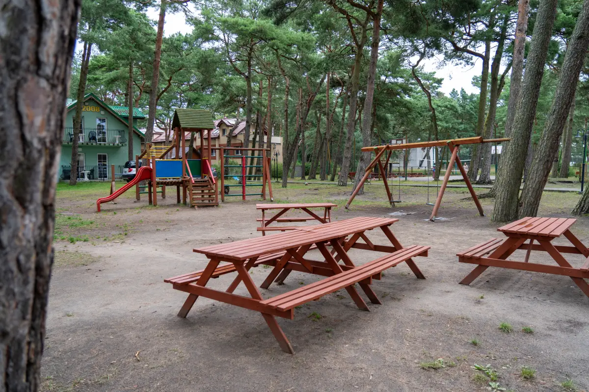 A playground with climbing frames and wooden picnic tables under pine trees at the complex