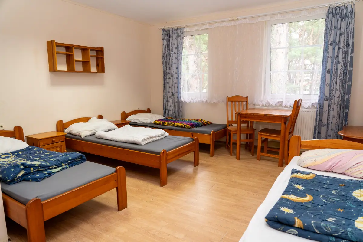A bedroom with wooden single beds, a table and chairs and a curtained window