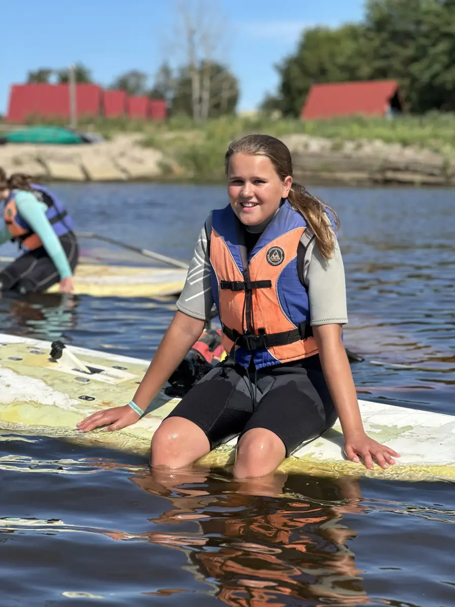 A girl in a buoyancy aid sitting on a paddle board out on Lake Resko