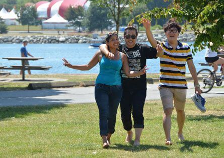 Three students walking together through a park by the water in Vancouver on a sunny day