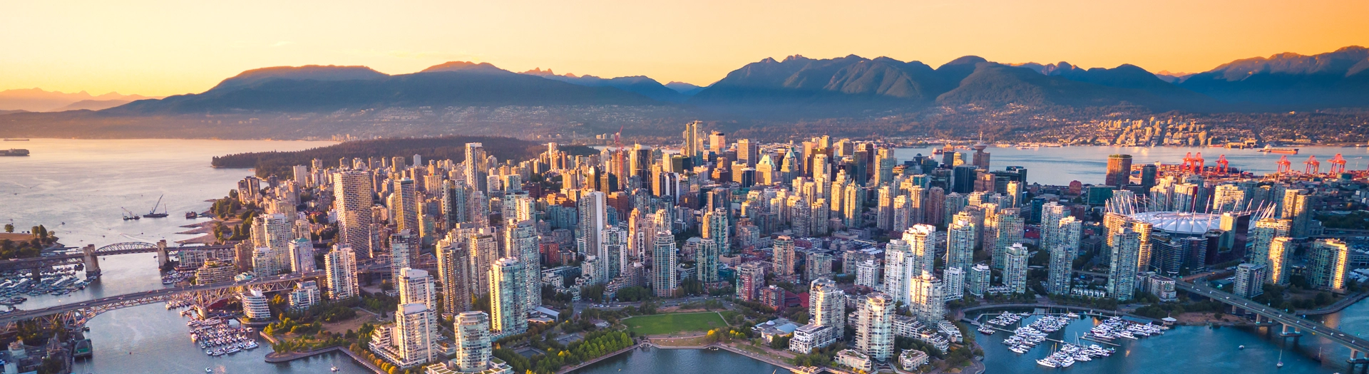 Aerial view of downtown Vancouver at dusk, with the harbour and the coastal mountains behind the towers