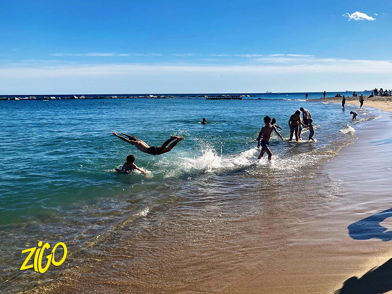 Young people playing in the shallow water of a Barcelona beach on a bright day