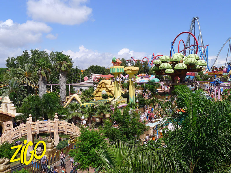 Themed pavilions and roller coaster tracks rising above tropical planting at the theme park