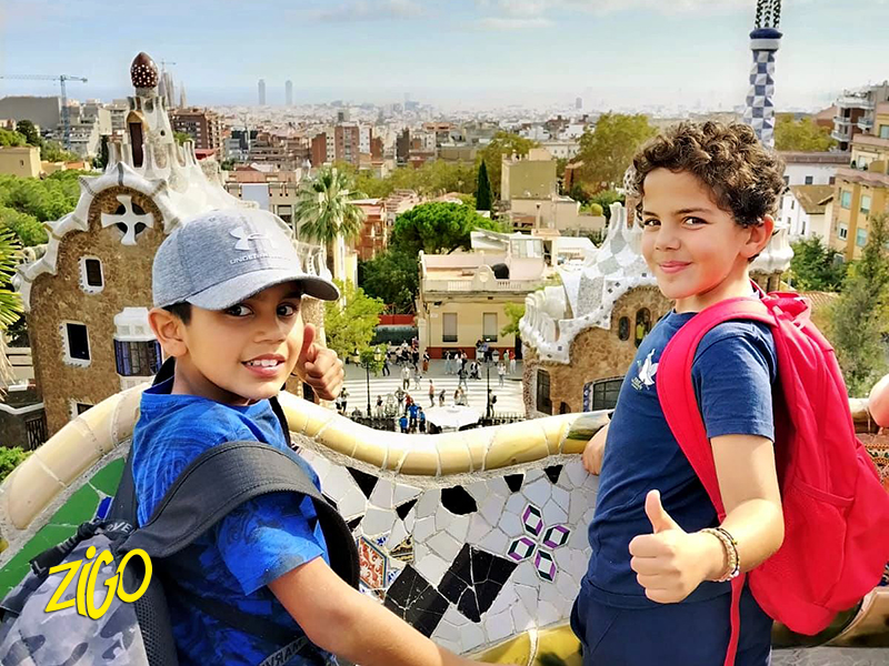 Two participants leaning on the mosaic parapet of Park Güell with the city behind them
