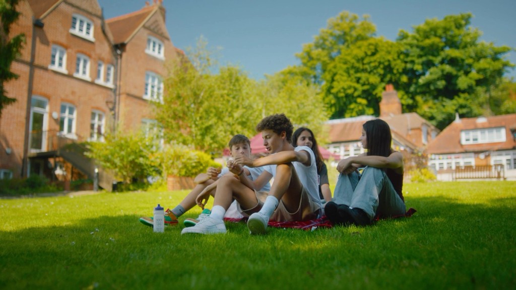 Teenagers relaxing on the campus lawn with the school buildings and trees behind them, Mill Hill, London