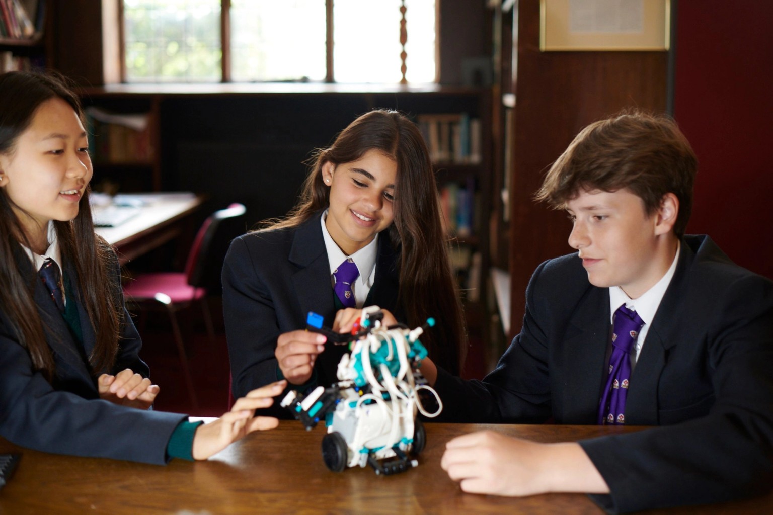 Three students in school uniform building a robot at a table in a wood-panelled room, Mill Hill School, London