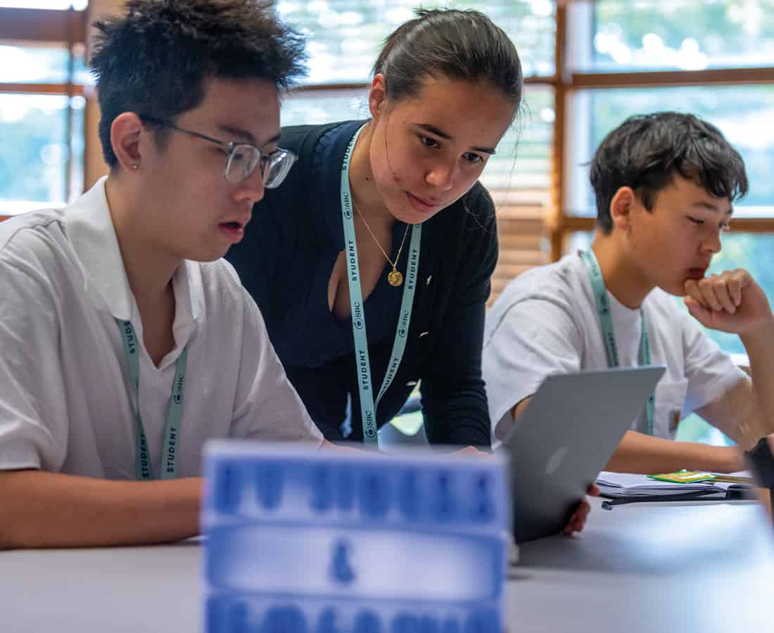 Three students concentrate as they work together on their laptops in an academic class