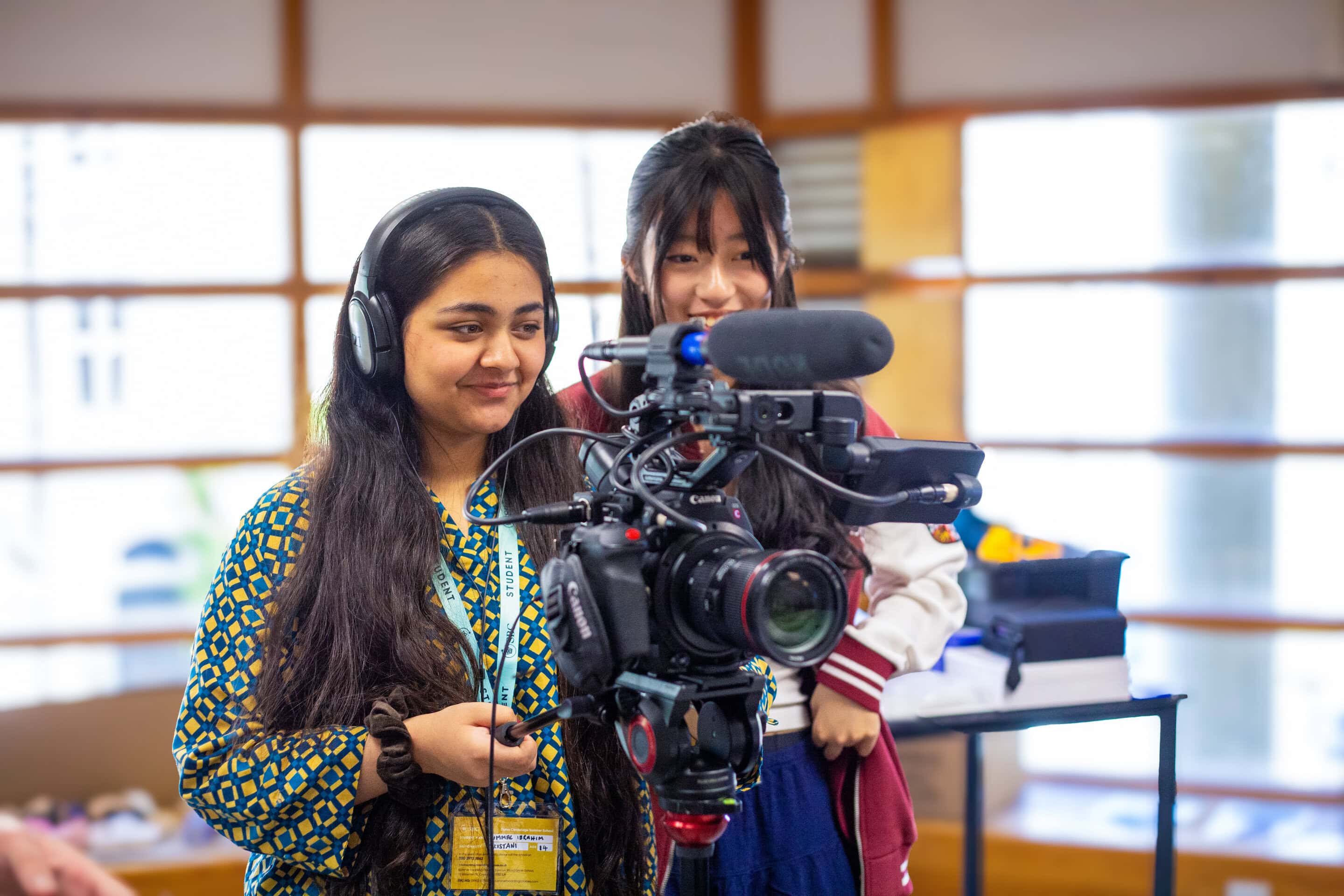 Two students operate a professional video camera and boom microphone indoors