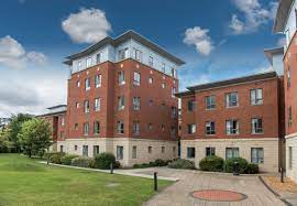 A modern red-brick student residence building with lawns and a paved path outside