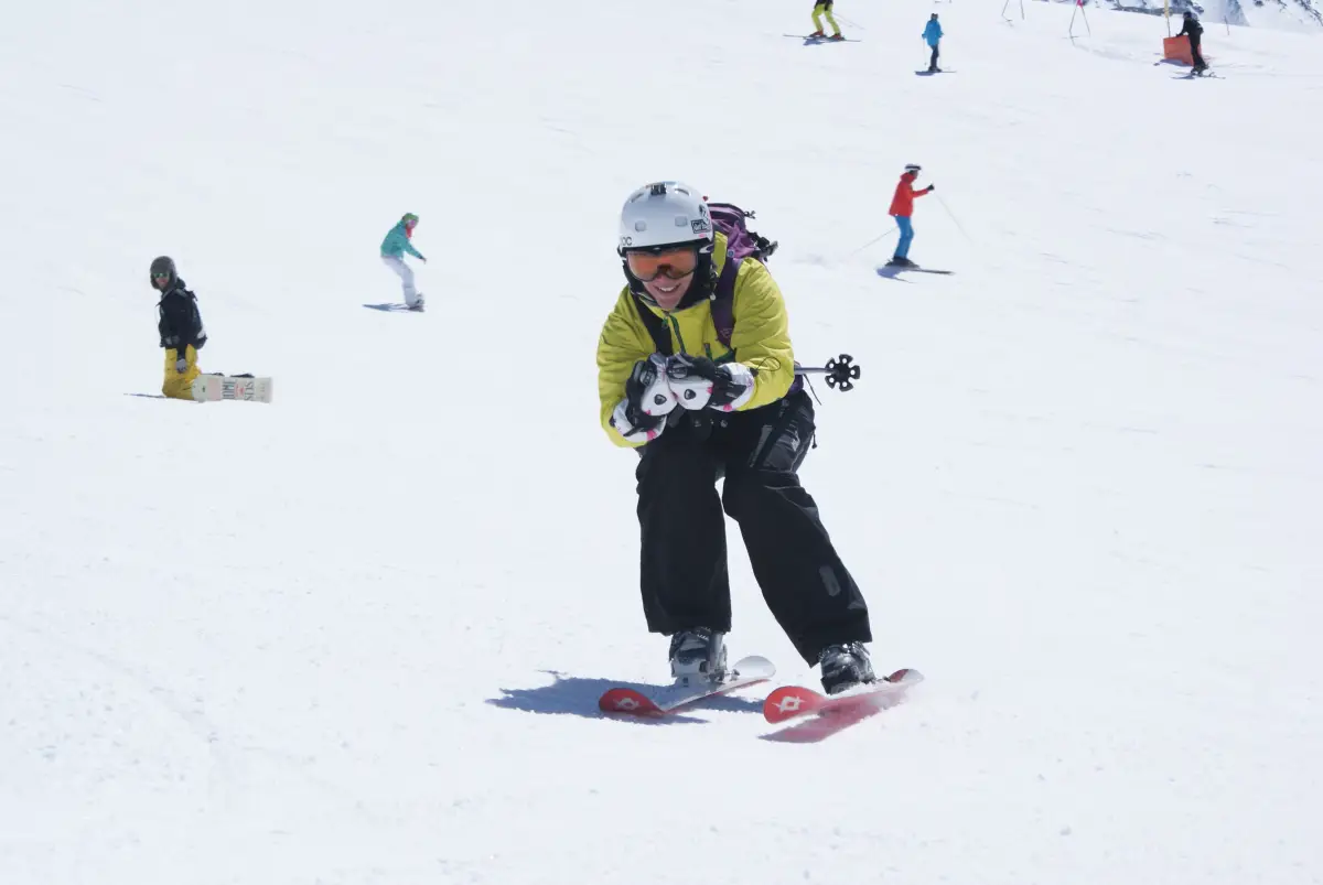 A young skier in a helmet turning on a broad, gentle piste with other skiers further up