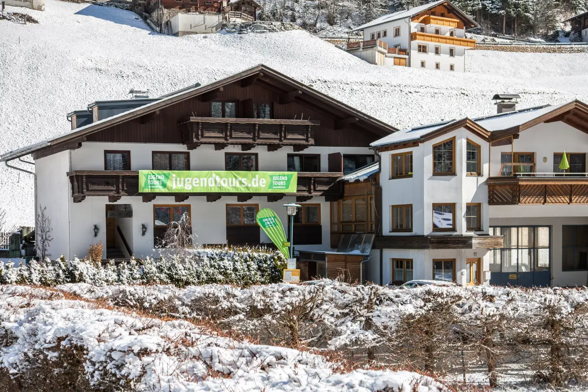 A traditional alpine guest house with a dark timber balcony front, standing in deep snow