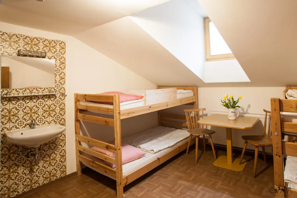 A simple room with wooden bunk beds, a washbasin and a small table under a sloping ceiling