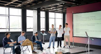 Students presenting a business pitch in front of a screen to a seated panel, InvestIN Entrepreneur Summer Experience in London