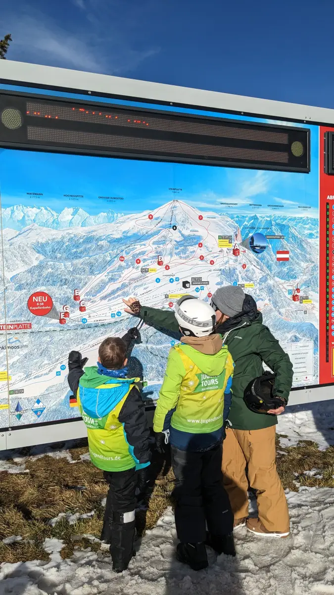 A group in Jugendtours bibs reading the illustrated piste map of the ski area