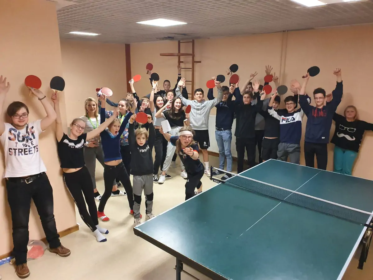 A large group celebrating around a table-tennis table in an indoor games room