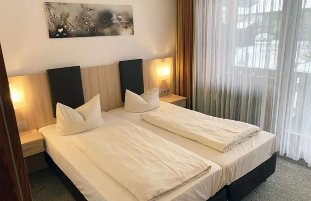 A bedroom with two single beds pushed together, bedside lamps and light curtains