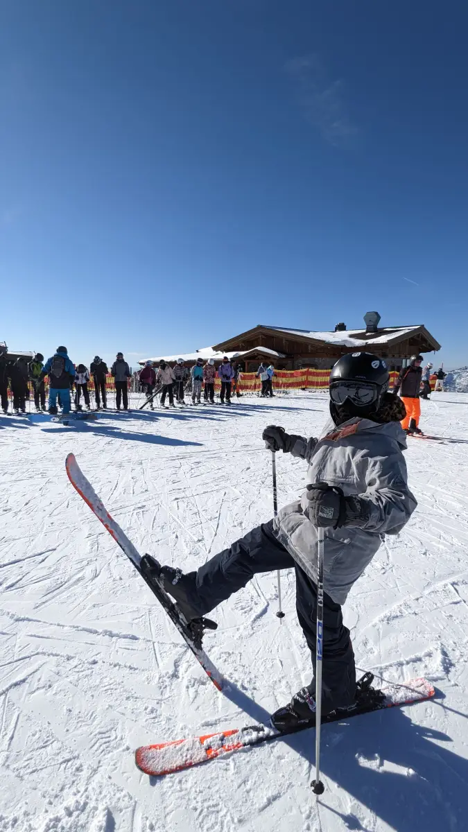 A young skier turning on a groomed piste with a wooden mountain hut behind