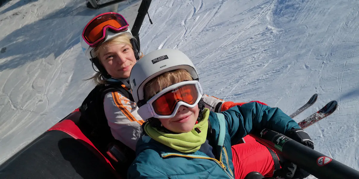 Two young snow-sports participants in helmets and ski goggles sitting in the snow