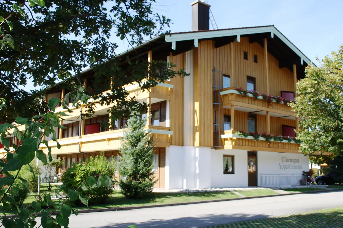 A wooden-fronted alpine building among trees, photographed in the green season