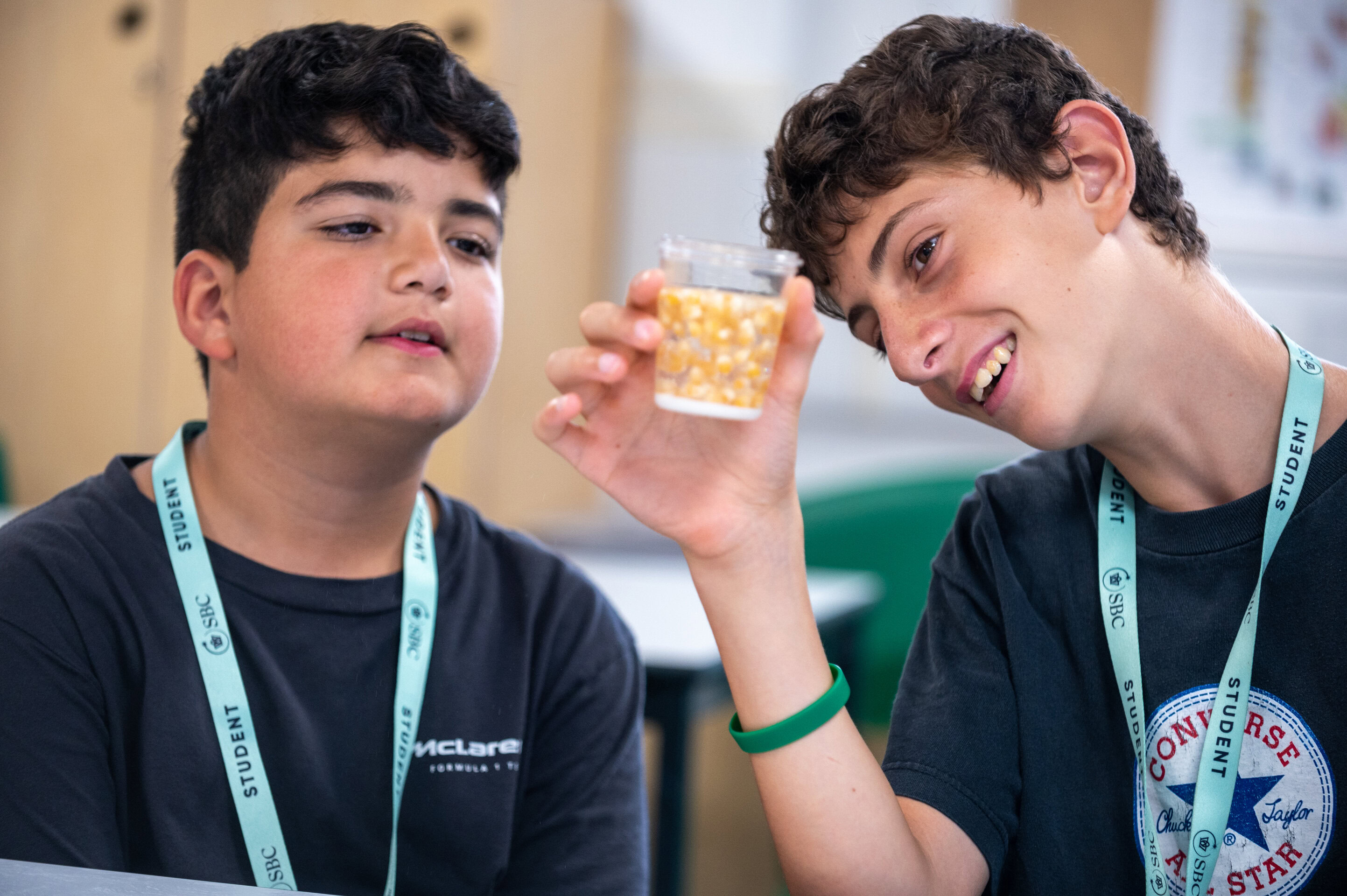 Two students smile while holding a beaker of yellow liquid during a science lesson
