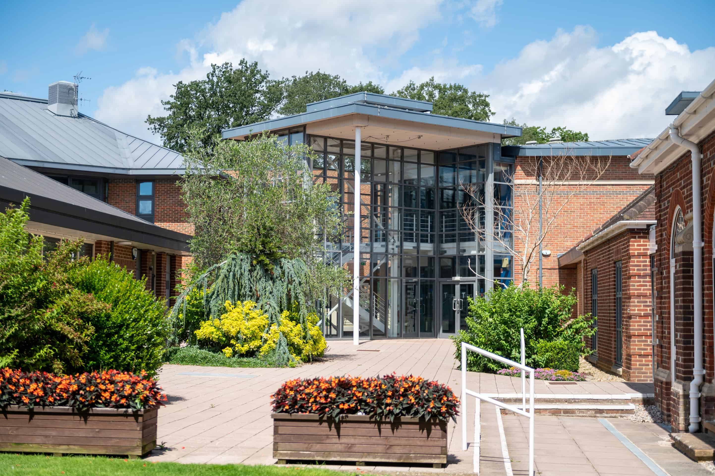 A modern glass-fronted school building with flower beds and a paved path outside