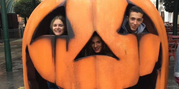 Three campers looking through the cut-outs of a giant carved pumpkin