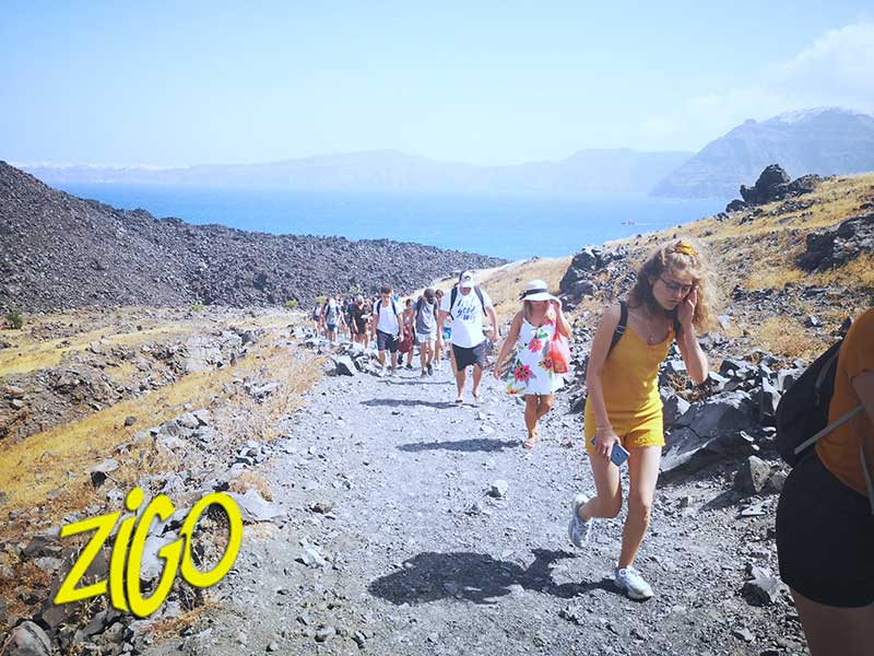 Line of young people walking up a bare volcanic slope with the sea behind them