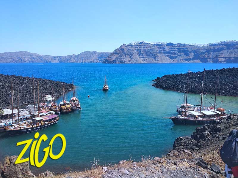 Small boats moored in the deep blue water of the caldera bay below the volcanic cliffs