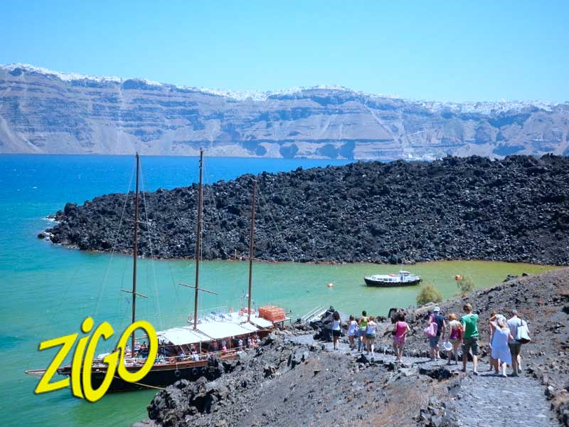 Traditional wooden caïque moored off a dark volcanic shore with people on the beach