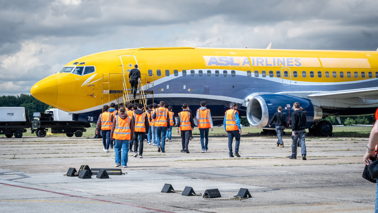Students in high-visibility vests boarding a Boeing jet at an airfield