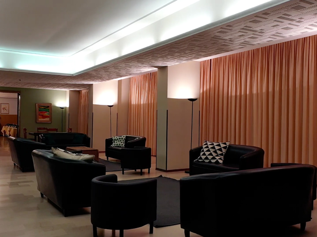 The main lounge at Villa Sancelso, with dark sofas and armchairs set on a pale floor against floor-length curtains and standing lamps
