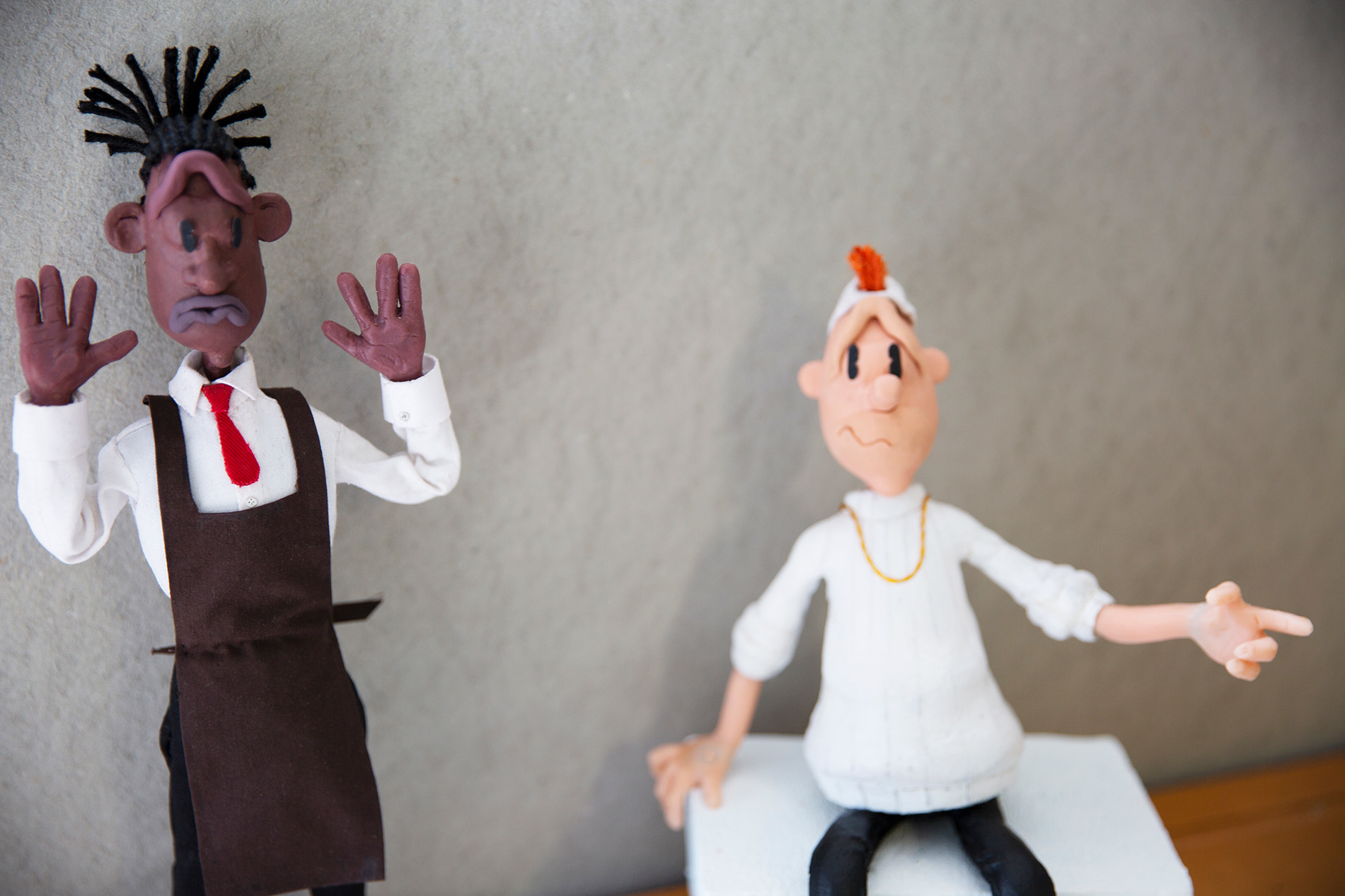 Two hand-modelled stop-motion puppets in shirts standing on a set against a plain backdrop