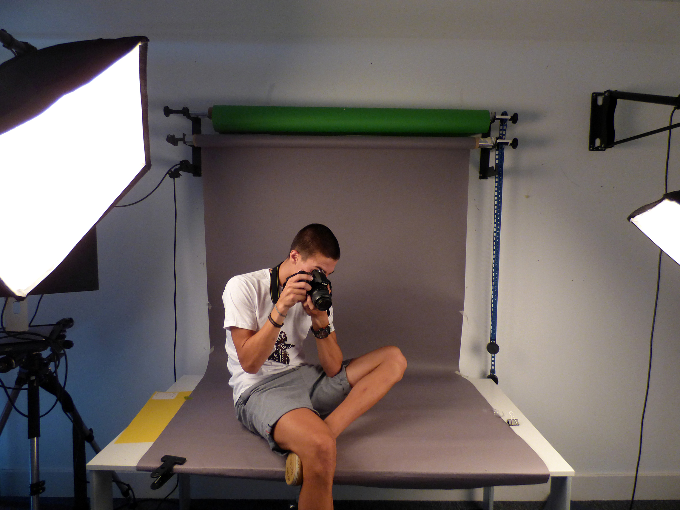 A participant with a camera sitting in a lit photographic studio in front of a green screen backdrop